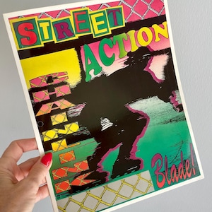 May include: A rectangular poster featuring the text STREET ACTION and Blade! in bold lettering. A black silhouette of a person on inline skates is centered against a green and yellow background with a chain-link fence pattern at the top and bottom.