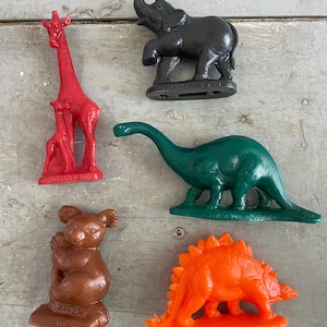 May include: A collection of colorful plastic animal figurines, including a red giraffe, a black elephant, a green dinosaur, a brown koala, and an orange stegosaurus. The figurines are on a weathered wooden surface.