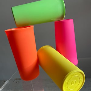 May include: Four plastic cups stacked on top of each other. The cups are in bright neon colors: green, orange, pink, and yellow. The yellow cup has the words "Tupperware" and "USA" printed on the bottom.