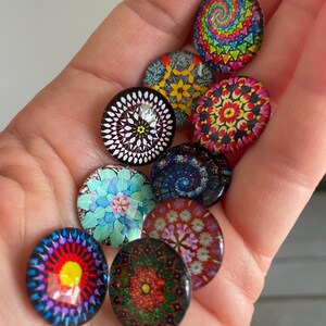 May include: A collection of ten round glass cabochons with colorful, intricate designs. The cabochons feature various patterns, including spirals, floral motifs, and geometric shapes, in a range of vibrant colors like red, blue, green, and yellow.