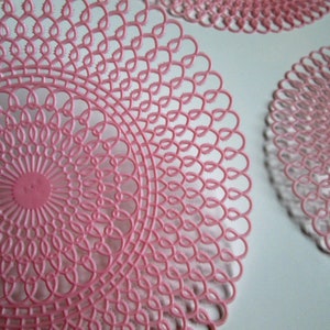 May include: Three pink crocheted doilies with a circular design. The doilies are made of a delicate, lacy material and have a scalloped edge.