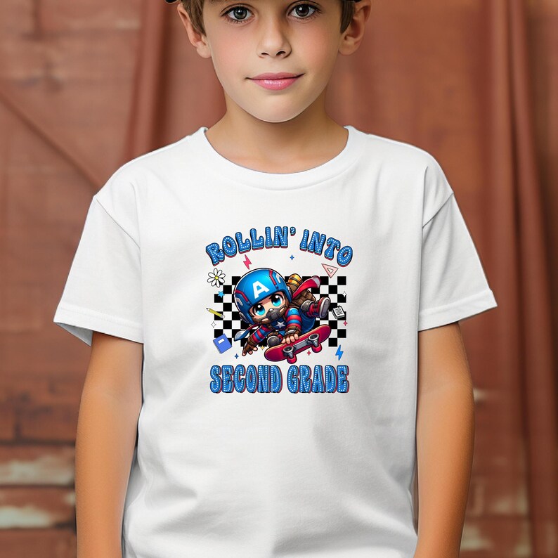 May include: White t-shirt with a graphic of a cartoon character on a skateboard, wearing a helmet with the letter "A". The text "ROLLIN' INTO SECOND GRADE" is in blue. The design includes a checkered background.