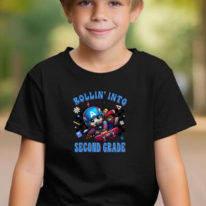 May include: Black t-shirt featuring a cartoon illustration of a character in a Captain America-style helmet riding a skateboard. The text "ROLLIN' INTO SECOND GRADE" is in blue and white.