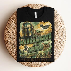 Puede incluir: Una camiseta negra con un estampado gr&aacute;fico de The Mandalorian y Grogu. El dise&ntilde;o incluye el texto "THE MANDALORIAN AND GROGU" y "THIS IS THE WAY" en letras verdes, junto con ilustraciones de una nave espacial, un AT-ST y varias criaturas.