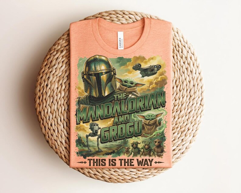 Puede incluir: Una camiseta color melocot&oacute;n con un estampado gr&aacute;fico de The Mandalorian y Grogu. El dise&ntilde;o incluye el texto "THE MANDALORIAN AND GROGU" y "THIS IS THE WAY" junto con ilustraciones de un personaje con casco, peque&ntilde;as criaturas verdes y una nave espacial.