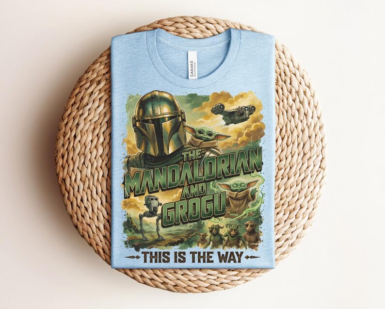 Puede incluir: Una camiseta azul claro con un estampado gr&aacute;fico de The Mandalorian y Grogu. El dise&ntilde;o incluye el texto "THE MANDALORIAN AND GROGU" y "THIS IS THE WAY" junto con ilustraciones de un personaje con casco, una peque&ntilde;a criatura verde y una nave espacial.