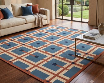 May include: A rectangular area rug featuring a geometric pattern of blue and dark blue squares connected by terracotta-colored lines on a cream background. The rug is placed on a dark wood floor in a room with a beige sofa and a marble-topped table.