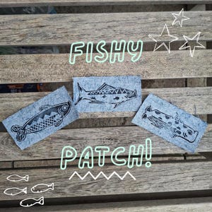 May include: Three rectangular denim patches featuring black ink-stamped fish illustrations. The text FISHY PATCH! is overlaid in light green, accompanied by three star outlines and four small fish icons at the bottom of the image.