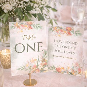 Può includere: Allestimento tavola nuziale con biglietti floreali. Un biglietto recita "Table ONE" in verde. L'altro biglietto recita "I HAVE FOUND THE ONE MY SOUL LOVES SONG OF SOLOMON 3:4". Entrambi i biglietti hanno accenti floreali.