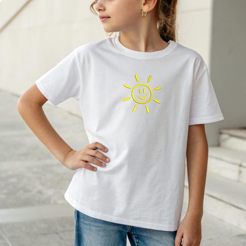 May include: White t-shirt featuring a yellow smiling sun graphic. The short-sleeved shirt is made of a soft material and is suitable for everyday wear. The sun design has a 3D effect.