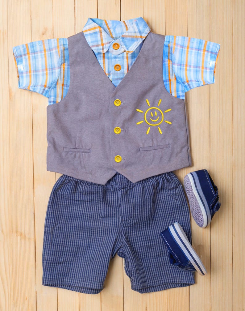 May include: A baby boy's outfit set on a wooden surface. The set includes a blue and orange plaid short-sleeved shirt, a gray vest with a yellow sun graphic, blue striped shorts, and navy blue shoes.