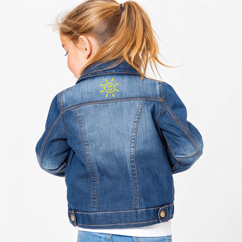 May include: A blue denim jacket with a yellow smiling sun design on the back. The jacket has a classic design with button closures and pockets. The denim is a medium wash, and the jacket appears to be for a child.