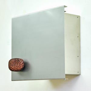May include: A silver metal wall-mounted cabinet with a textured, copper-colored knob. The cabinet has a rectangular shape with a hinged door. The design is minimalist and modern, suitable for storage.