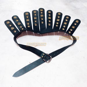 May include: Black leather belt with a unique design. The belt features a series of black leather finger-like extensions, each adorned with gold-colored studs. The belt has a silver buckle and the text "BOOTSTATION".