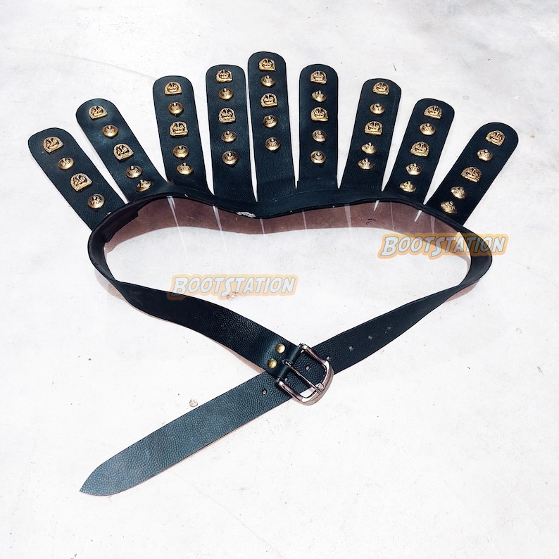 May include: Black leather belt with a unique design. The belt features a series of black leather finger-like extensions, each adorned with gold-colored studs. The belt has a silver buckle and the text "BOOTSTATION".