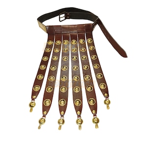 May include: A brown leather Roman belt with gold-colored accents. The belt features a black buckle and multiple leather straps adorned with gold medallions and decorative gold pendants at the ends. A historical costume accessory.