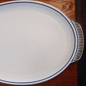 May include: A white ceramic serving platter with a blue and brown rim. The platter has a slightly raised edge and a smooth surface.