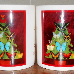 Puede incluir: Dos tazas de cerámica blanca con un borde rojo y un diseño de árbol de Navidad con un árbol verde decorado con mariposas de colores. El árbol está en una maceta roja.