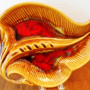 May include: A vintage ceramic leaf-shaped dish with a glossy finish. The dish features a warm, golden-brown exterior with a ribbed texture and a vibrant red interior. The decorative piece is likely for serving or display.