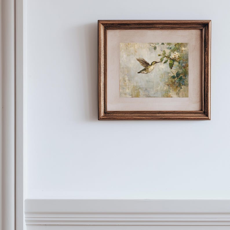 K&ouml;nnte beinhalten: Ein gerahmtes Kunstwerk mit einem Kolibri im Flug, der sich einer bl&uuml;henden Zweig n&auml;hert. Das Gem&auml;lde hat eine weiche, ged&auml;mpfte Farbpalette mit Gr&uuml;nt&ouml;nen, Beige und Braun. Der Rahmen ist in einem warmen, dunklen Braun gehalten.