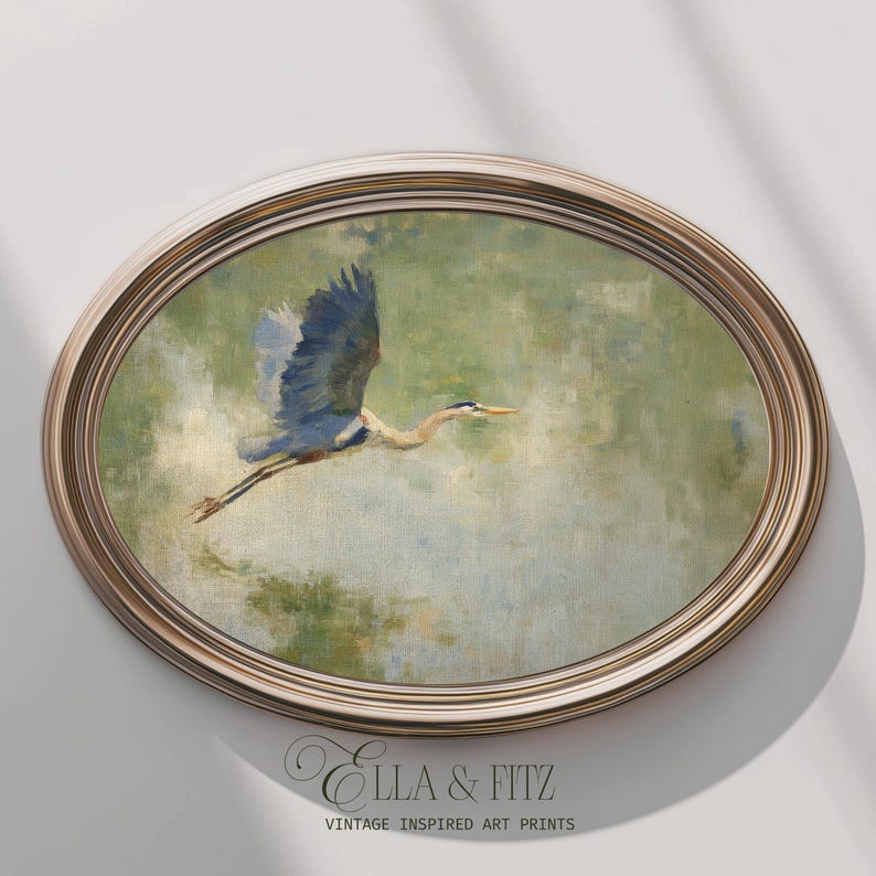 May include: An oval framed print featuring a blue heron in flight. The artwork has a vintage aesthetic with a muted color palette of greens, blues, and browns. The frame is a light brown color. The text "Ella & Fitz Vintage Inspired Art Prints" is at the bottom.