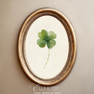 May include: A watercolour painting of a four-leaf clover in a gold oval frame. The clover is a vibrant green, set against a cream-coloured background. The frame has an ornate, textured design. The text "ELLA & FITZ" and "VINTAGE INSPIRED ART PRINTS" is at the bottom.
