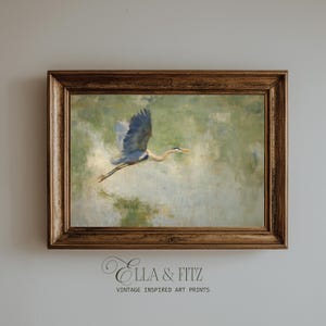 May include: A framed vintage-inspired art print featuring a blue heron in flight. The artwork has a soft, painterly style with a muted green and blue color palette. The frame is a warm, ornate brown. The text "Ella & Fitz" and "Vintage Inspired Art Prints" is visible.