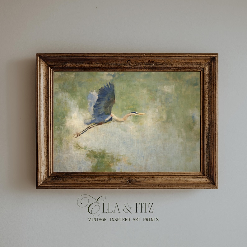 May include: A framed vintage-inspired art print featuring a blue heron in flight. The artwork has a soft, painterly style with a muted green and blue color palette. The frame is a warm, ornate brown. The text "Ella & Fitz" and "Vintage Inspired Art Prints" is visible.