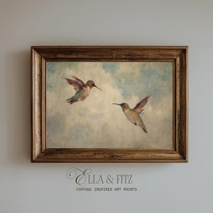 May include: A framed vintage-style art print showing two hummingbirds in flight against a cloudy sky. The birds have green, red, and brown plumage. The frame is a dark, ornate gold colour. The text "Ella & Fitz Vintage Inspired Art Prints" is at the bottom.
