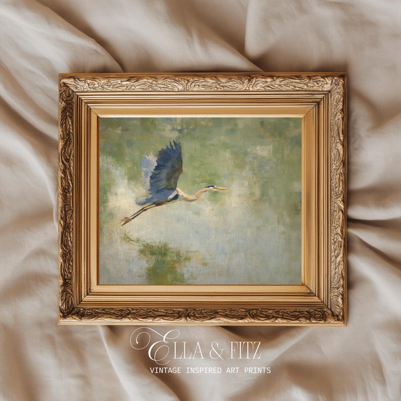 May include: A framed vintage-inspired art print featuring a blue heron in flight. The artwork is set against a soft green and blue background, framed in a gold ornate frame. The print is labeled "Ella & Fitz, Vintage Inspired Art Prints."