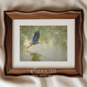 May include: A framed art print featuring a blue heron in flight against a soft green and beige background. The bird's wings are spread, and its long neck is extended. The frame is a dark wood with a wavy edge. The print is labeled "Ella & Fitz Vintage Inspired Art Prints."