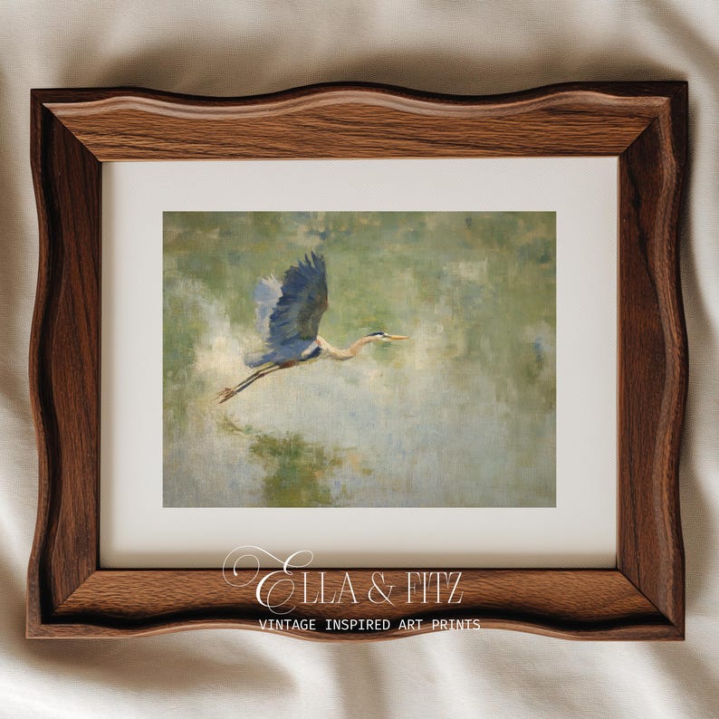 May include: A framed art print featuring a blue heron in flight against a soft green and beige background. The bird's wings are spread, and its long neck is extended. The frame is a dark wood with a wavy edge. The print is labeled "Ella & Fitz Vintage Inspired Art Prints."