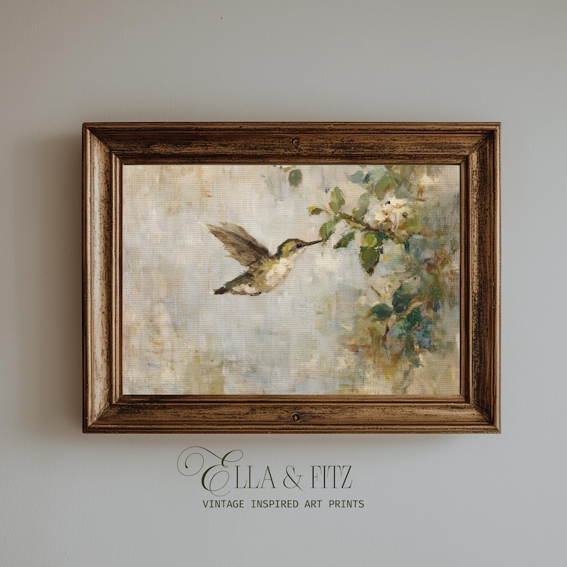 K&ouml;nnte beinhalten: Gerahmter Kunstdruck im Vintage-Stil mit einem Kolibri im Flug, der sich einem bl&uuml;henden Zweig n&auml;hert. Das Kunstwerk hat einen weichen, malerischen Stil mit ged&auml;mpften T&ouml;nen von Gr&uuml;n, Braun und Wei&szlig;. Der Rahmen ist warmbraun.