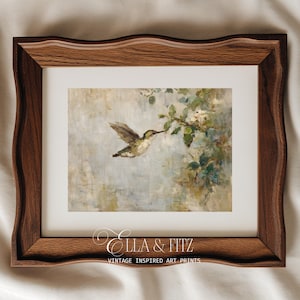 K&ouml;nnte beinhalten: Ein gerahmter Kunstdruck mit einem Kolibri im Flug, der nach einem bl&uuml;henden Zweig greift. Das Kunstwerk hat einen weichen, malerischen Stil mit ged&auml;mpften Blau-, Gr&uuml;n- und Wei&szlig;t&ouml;nen. Der Rahmen ist aus dunklem Holz mit dekorativem Rand. Der Text "Ella & Fitz" und "Vintage Inspired Art Prints" befindet sich unten.