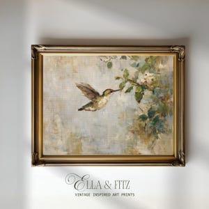 Puede incluir: Una impresión artística enmarcada de estilo vintage que representa un colibrí en vuelo, alcanzando una rama florida. La obra de arte tiene una paleta de colores suaves y apagados con un marco dorado. El texto "Ella & Fitz" está en la parte inferior.