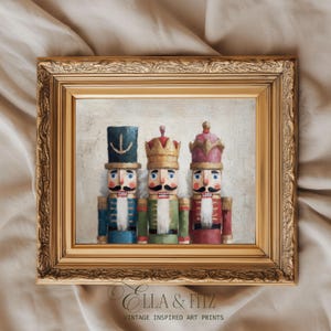 May include: A framed art print featuring three nutcracker figures in blue, green, and red uniforms with gold crowns and black mustaches, set against a textured off-white background, enclosed in an ornate gold-coloured rectangular frame.
