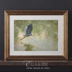 May include: Framed art print featuring a blue heron in flight against a soft green and white background. The artwork is presented in a gold-toned frame with a white mat. The print is labeled "Ella & Fitz Vintage Inspired Art Prints."