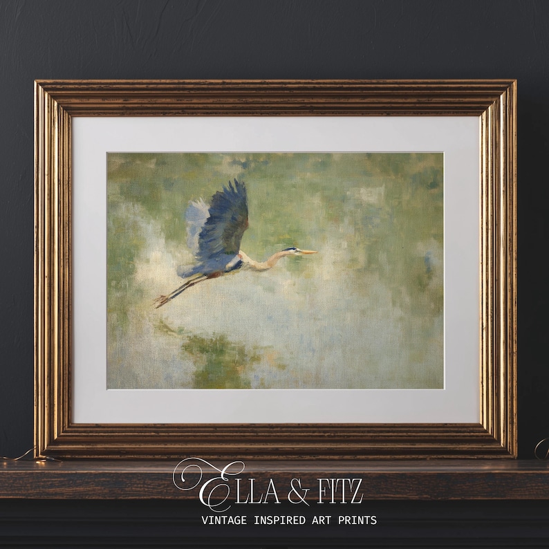 May include: Framed art print featuring a blue heron in flight against a soft green and white background. The artwork is presented in a gold-toned frame with a white mat. The print is labeled "Ella & Fitz Vintage Inspired Art Prints."
