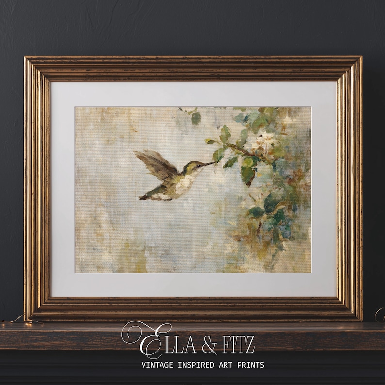 K&ouml;nnte beinhalten: Ein gerahmter Kunstdruck mit einem Kolibri im Flug, der sich einem bl&uuml;henden Zweig n&auml;hert. Das Kunstwerk hat einen weichen, malerischen Stil mit ged&auml;mpften T&ouml;nen von Gr&uuml;n, Braun und Blau. Der Rahmen ist goldfarben und der Druck tr&auml;gt die Aufschrift "Ella & Fitz Vintage Inspired Art Prints."