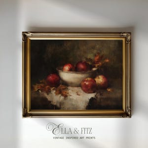 Peut inclure: Une peinture à l'huile encadrée représentant une nature morte de pommes rouges dans un bol blanc posé sur un tissu blanc avec des feuilles d'automne éparpillées. L'œuvre est dans un cadre doré orné. Le texte ELLA & FITZ VINTAGE INSPIRED ART PRINTS apparaît en dessous.