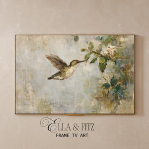 Könnte beinhalten: Gerahmtes Kunstwerk mit einem Kolibri im Flug, der sich einem blühenden Zweig nähert. Das Gemälde hat einen weichen, impressionistischen Stil mit gedämpften Grün-, Braun- und Blautönen. Der Rahmen ist goldfarben. Der Text "Ella & Fitz FRAME TV ART" steht unten.