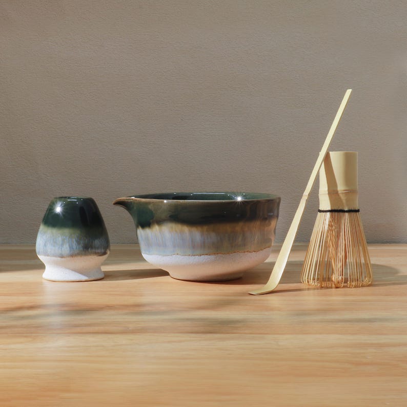 Op de afbeelding: Een matcha-theeset met een keramische kom, een kleine beker, een bamboe klopper en een bamboe lepel. De keramische stukken hebben een kleurengradi&euml;nt van wit, blauw en groen. De klopper en lepel zijn gemaakt van lichtgekleurd bamboe.