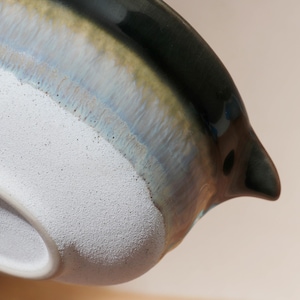 Op de afbeelding: Close-up van een keramische kan met een donkergroene, blauwe en bruine geglazuurde buitenkant. De kan heeft een witte, getextureerde binnenkant en een tuit. Het glazuur cre&euml;ert een gradi&euml;nteffect.