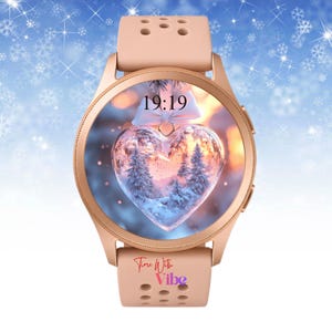Puede incluir: Reloj inteligente de oro rosa con una pantalla en forma de corazón que muestra una escena invernal con árboles y la hora 19:19. El reloj tiene una correa a juego y el texto "Time With Vibe" es visible en la correa.