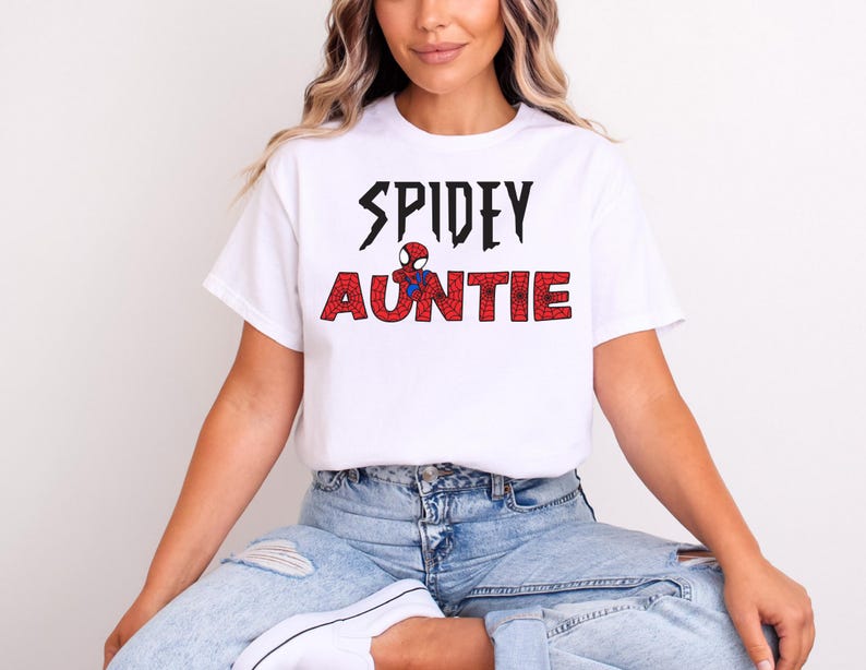 K&ouml;nnte beinhalten: Wei&szlig;es T-Shirt mit dem Text "SPIDEY AUNTIE" in Schwarz und Rot, mit einer Spider-Man-Grafik. Das Shirt ist aus einem weichen Material und eignet sich f&uuml;r Freizeitkleidung. Das Design ist mittig auf der Vorderseite des Shirts platziert.