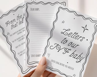 May include: A stack of white cards with black decorative borders and text. The cards read "Letters to our IVF baby" and "Dear Baby." One card reads "From the journey that led." The cards are held by a hand.