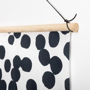 May include: A black and white wall hanging with a wood dowel and black string for hanging. The fabric features a repeating pattern of black circles on a white background.