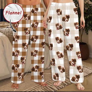 May include: Brown and white plaid flannel pajama pants featuring a repeating pattern of a dog's face. The pants have a relaxed fit and are made of a soft, cozy material. The image shows two pairs of the pajama pants.