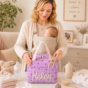 May include: A purple corduroy lunch bag featuring a small brown floral pattern and the name Helen embroidered in white script on the front pocket. The bag has two cream-colored fabric handles and a zipper closure with two small metal zipper pulls.