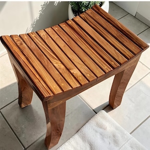 May include: A wooden bench with a slatted seat and curved legs. The bench is made of light brown wood and has a natural finish. The bench is approximately 46 cm long, 30 cm wide, and 41 cm high.